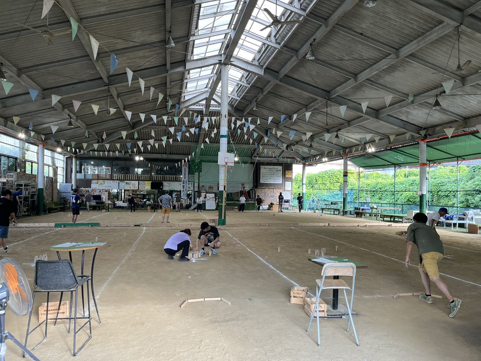 Mölkky courts marked out on sand under a high roof, with players setting up skittles